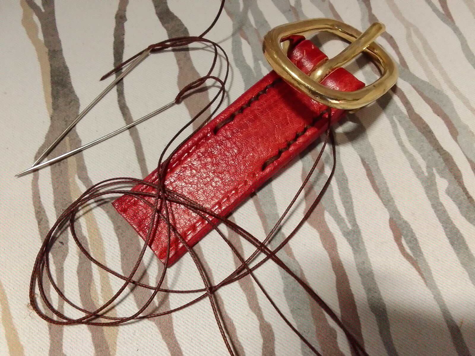 Couture manuelle d’une patte en cuir rouge avec bouclerie en laiton
